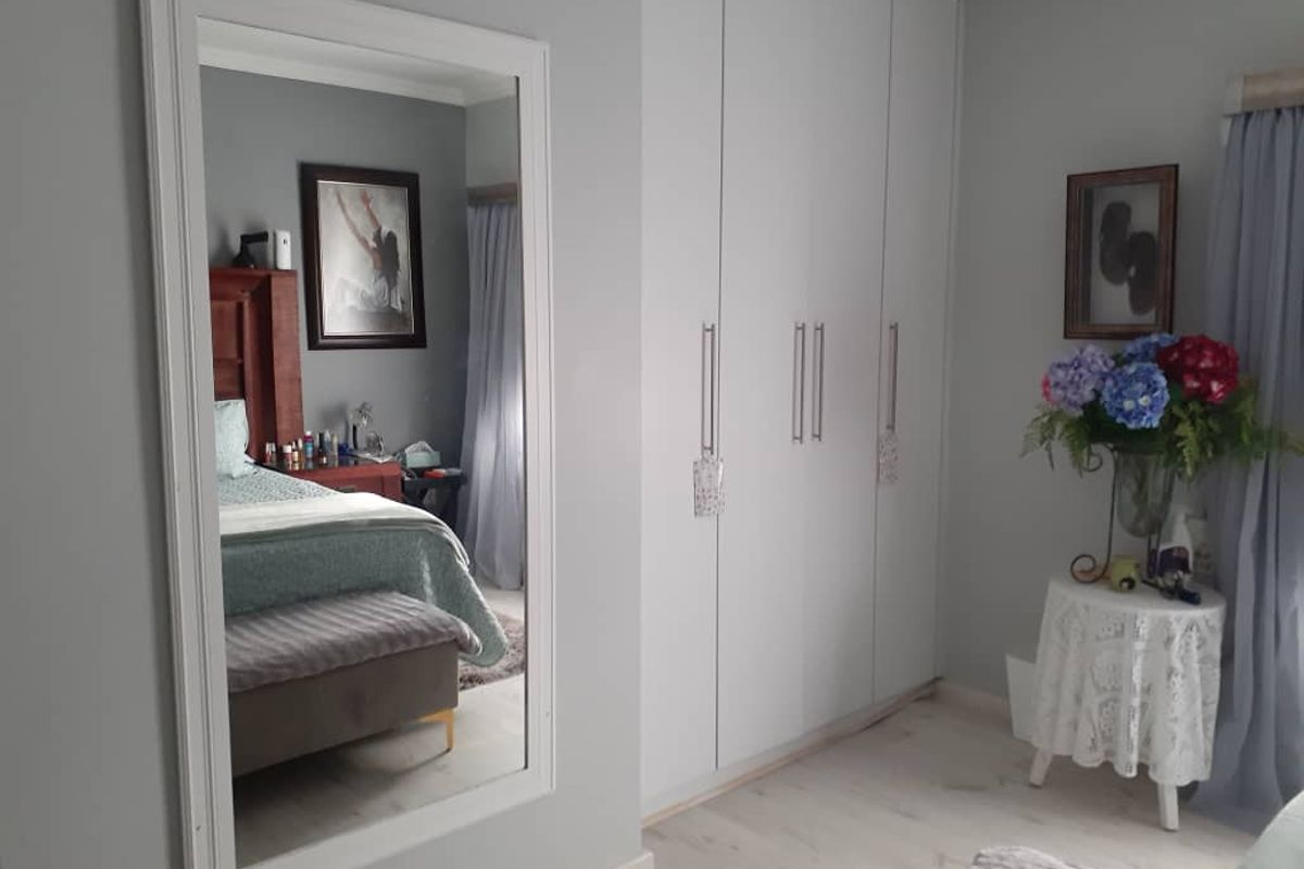 A well-maintained bedroom featuring light-toned laminate flooring and ample built-in cupboard storage, complemented by a large wall-mounted mirror.