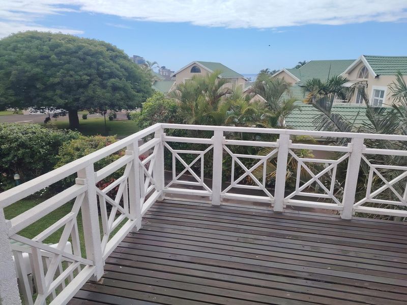An elevated timber balcony featuring a white decorative balustrade, offering views over the surrounding residential estate and greenery.