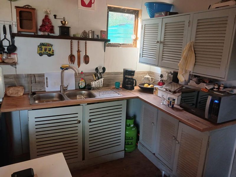 A compact kitchen featuring louvered cabinetry, timber countertops, a double bowl stainless steel sink, and tiled splashback, offering a functional prep area.