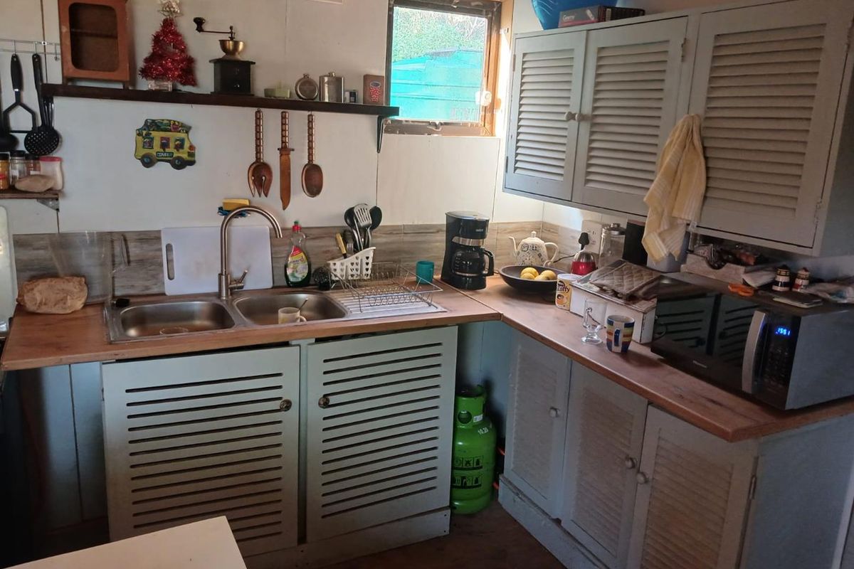 A compact kitchen featuring louvered cabinetry, timber countertops, a double bowl stainless steel sink, and tiled splashback, offering a functional prep area.