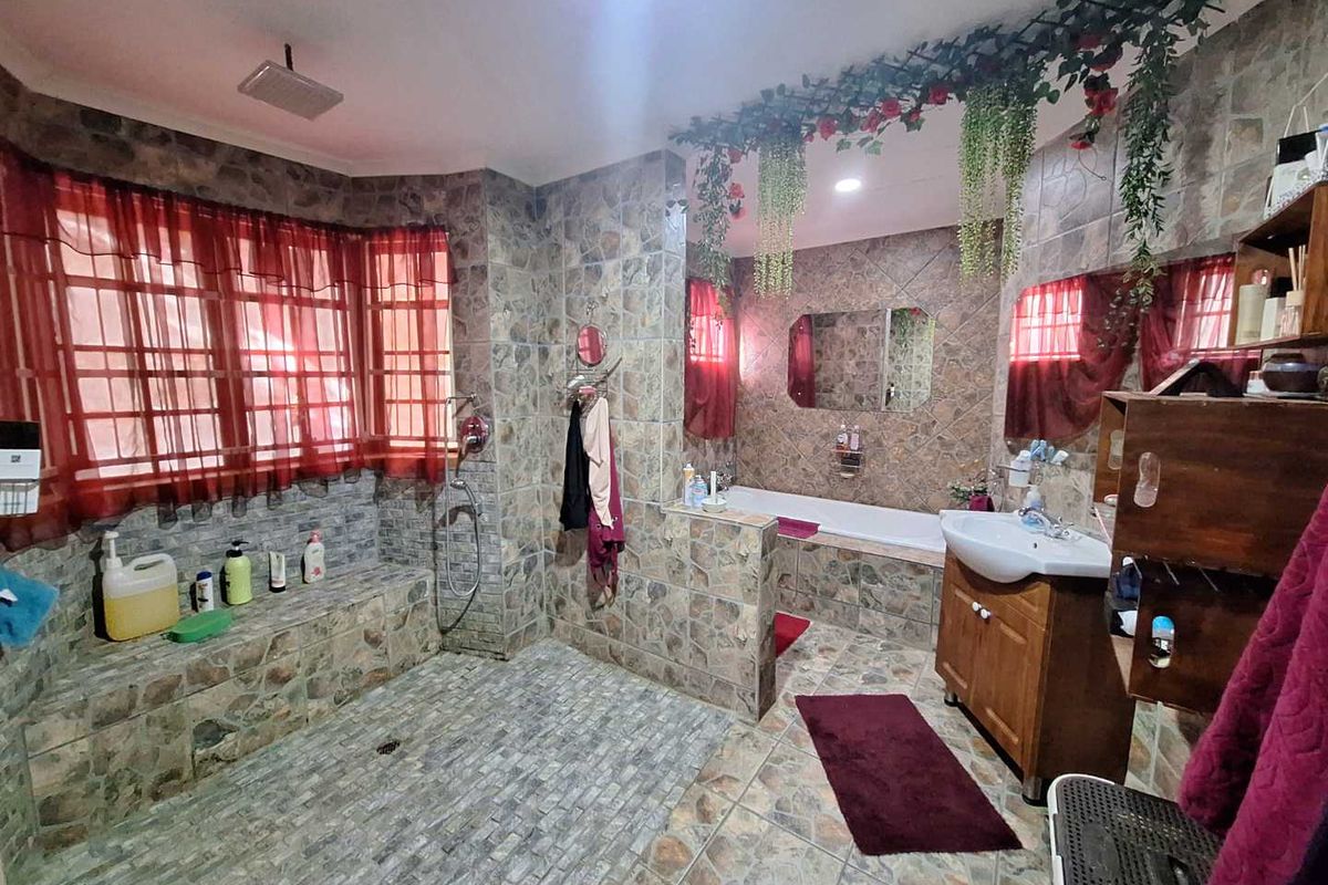 Spacious bathroom featuring a large walk-in shower area, built-in bathtub, and vanity unit with stone-style wall and floor tiling throughout.