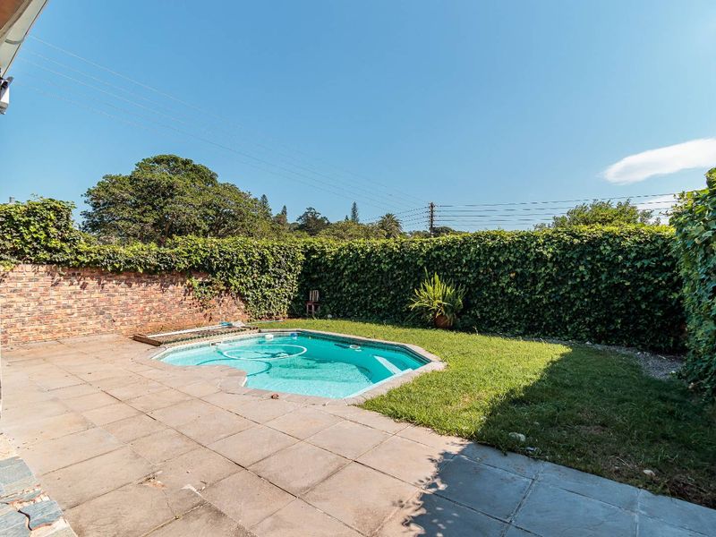 Outdoor pool area featuring a swimming pool, paved patio, and a brick boundary wall with established greenery.