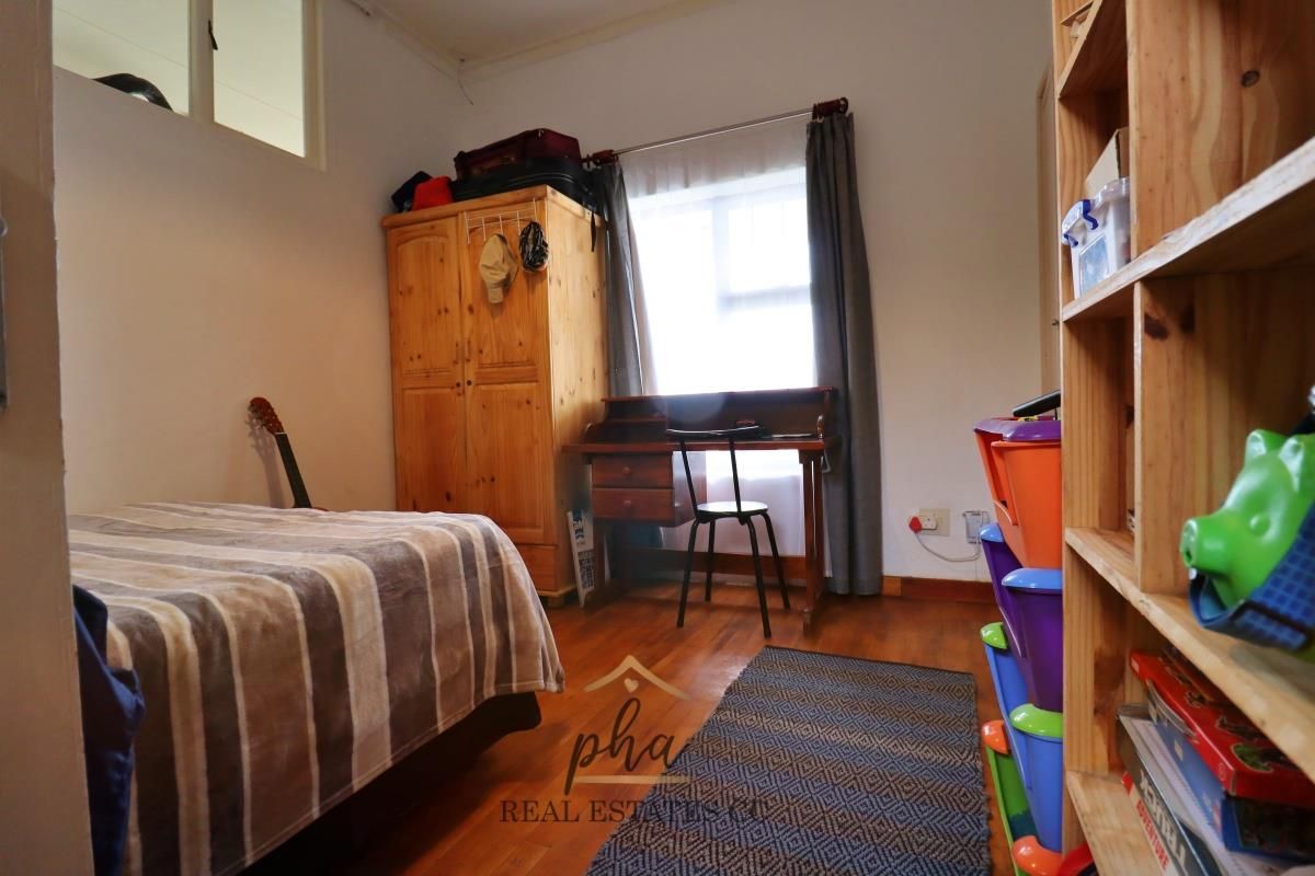 A functional bedroom featuring timber flooring, a window with curtain tracks, and a high-level transom window for additional natural light.