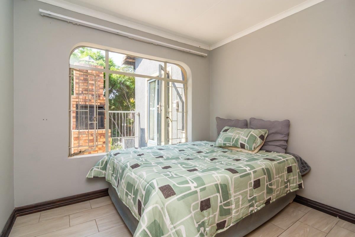 A bedroom featuring tiled flooring and an arched window with security bars, providing access to an outdoor area with a brick fireplace.