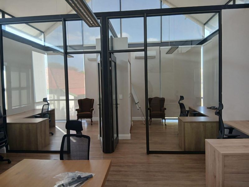 Modern office space featuring glass-partitioned private offices, laminate flooring, and high ceilings with integrated skylights and air conditioning.