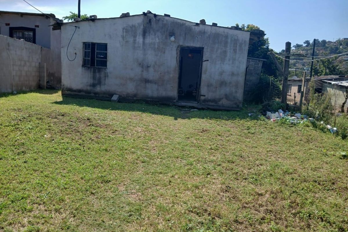 Rear view of a small detached dwelling showing significant exterior wall weathering and structural wear, set within a grassed yard area.