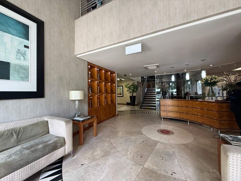 A professional office reception area featuring a curved wooden reception desk, built-in shelving, stone flooring, and a staircase leading to an upper level.