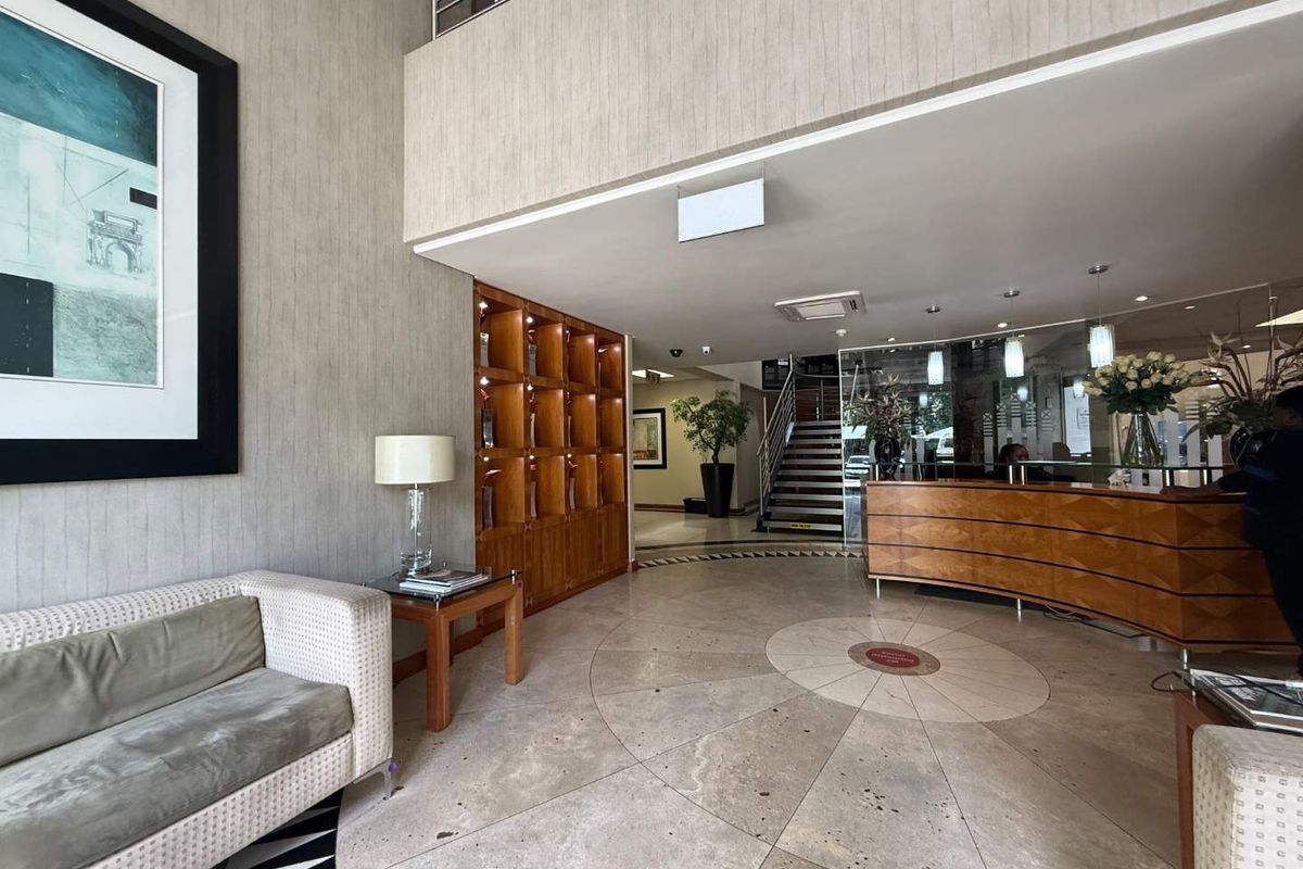 A professional office reception area featuring a curved wooden reception desk, built-in shelving, stone flooring, and a staircase leading to an upper level.