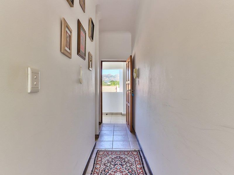 A bright, tiled hallway leading towards an exterior balcony with mountain views.