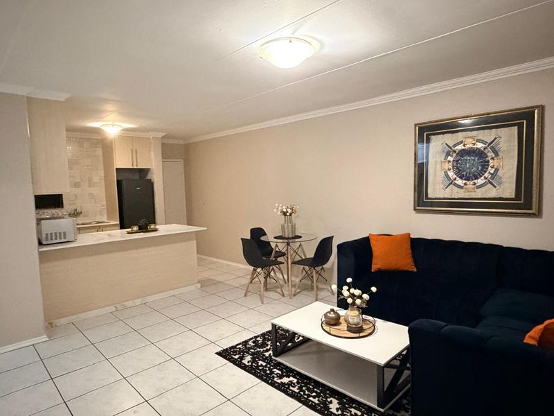 Open-plan living and dining area featuring a functional kitchen with a breakfast bar and neutral tiled flooring throughout.