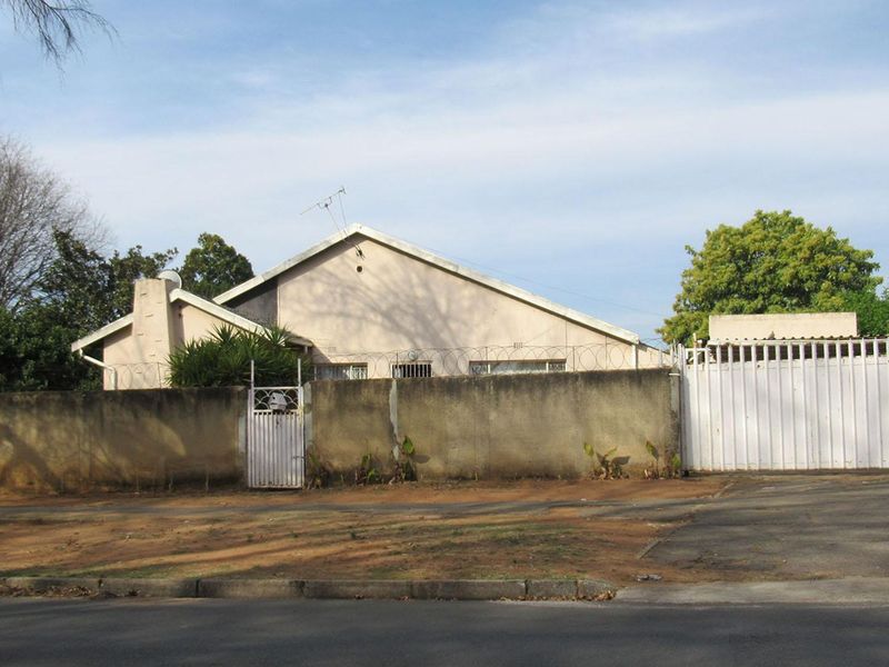 Front view of the property featuring a perimeter wall with security razor wire, a metal driveway gate, and a pedestrian entrance.