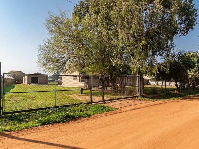 Street view of a small holding property featuring a dirt road access, chain-link perimeter fencing, and a detached garage structure.
