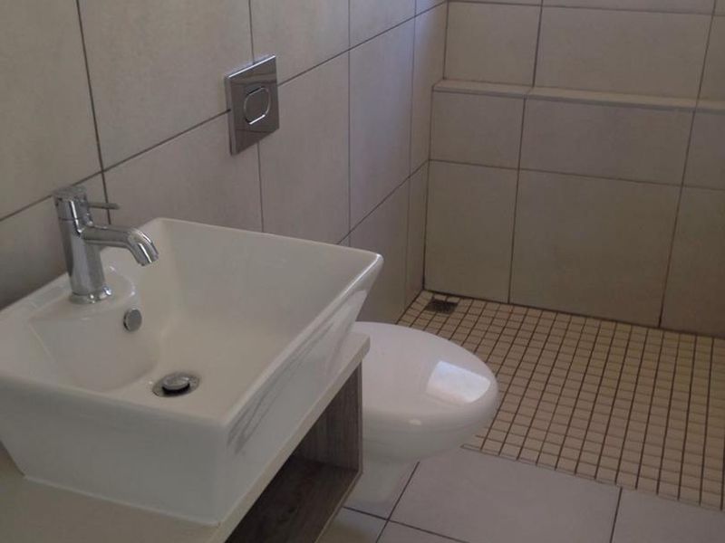 A modern, clean bathroom featuring a wall-mounted basin, wall-hung toilet with a flush plate, and tiled finishes throughout.