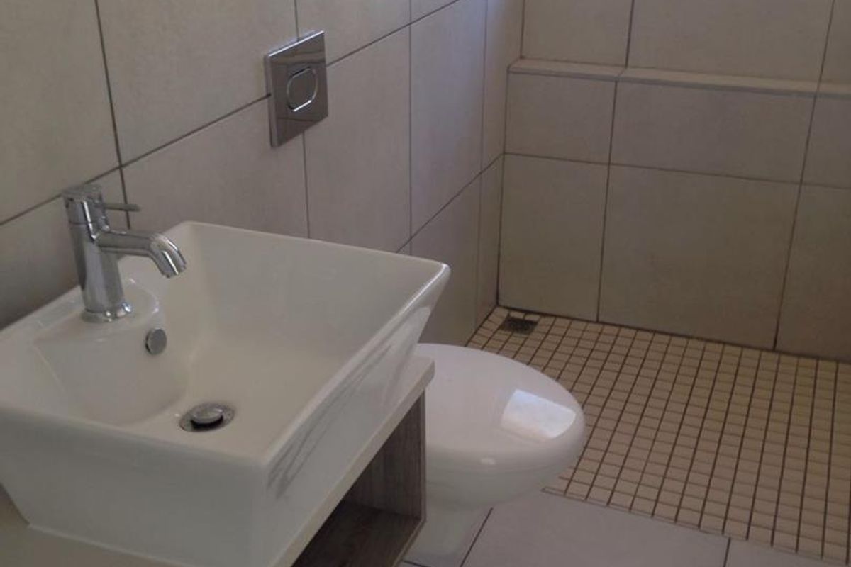 A modern, clean bathroom featuring a wall-mounted basin, wall-hung toilet with a flush plate, and tiled finishes throughout.