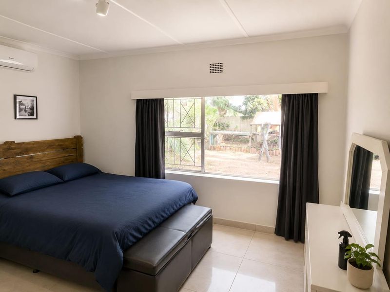 A well-maintained bedroom featuring tiled flooring, an air conditioning unit, and a large window with security bars overlooking the rear garden.