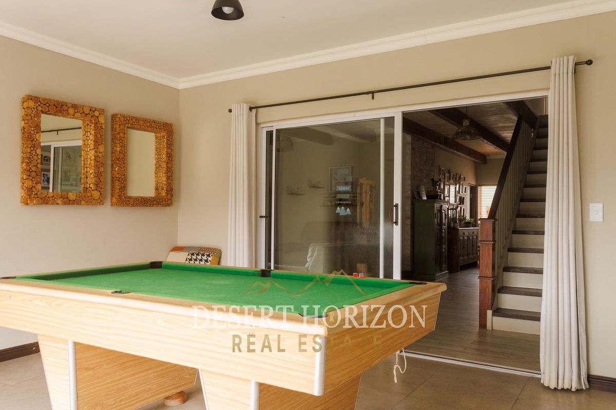 A spacious living area featuring tiled flooring, sliding glass doors leading to an adjacent room, and a staircase with a wooden handrail.