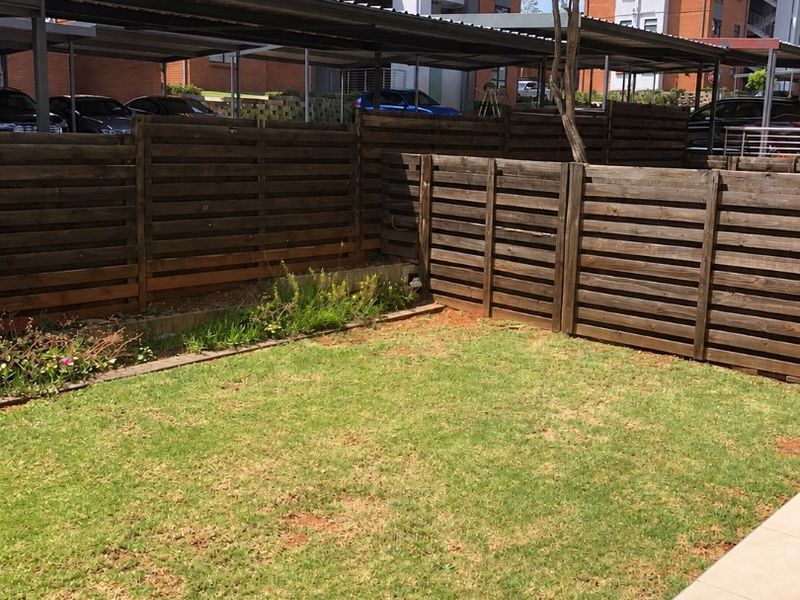 A private rear garden area featuring a small lawn, timber slat fencing, and an adjoining tiled patio space.