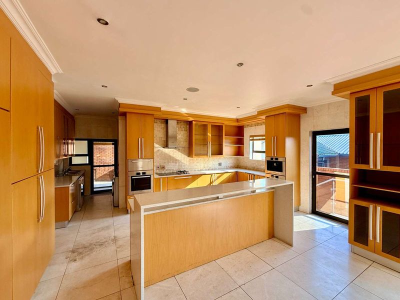 Spacious kitchen featuring light wood cabinetry, stone countertops, built-in appliances, and tiled flooring with direct access to an outdoor area.