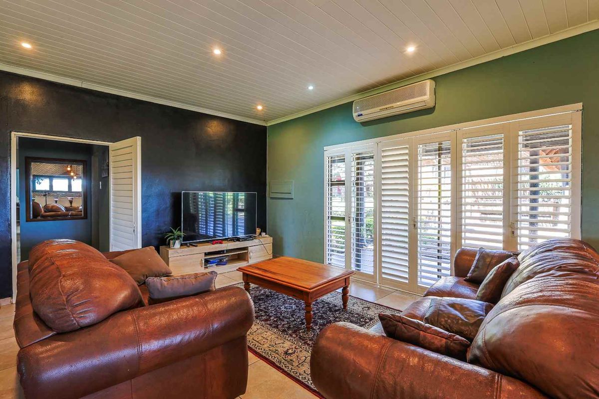 A comfortable living room featuring tiled flooring, recessed ceiling lighting, and white plantation shutters opening to the exterior.