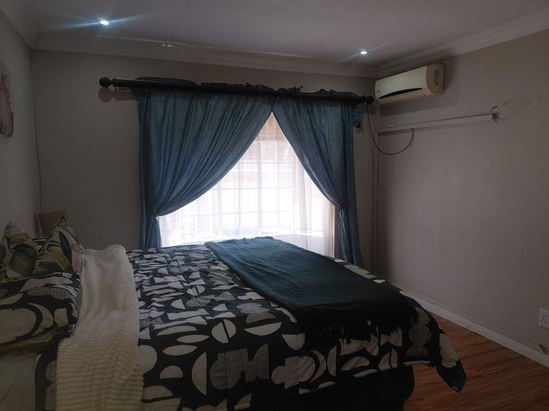 A bedroom featuring laminate flooring, recessed downlighting, and a wall-mounted split-system air conditioner unit.