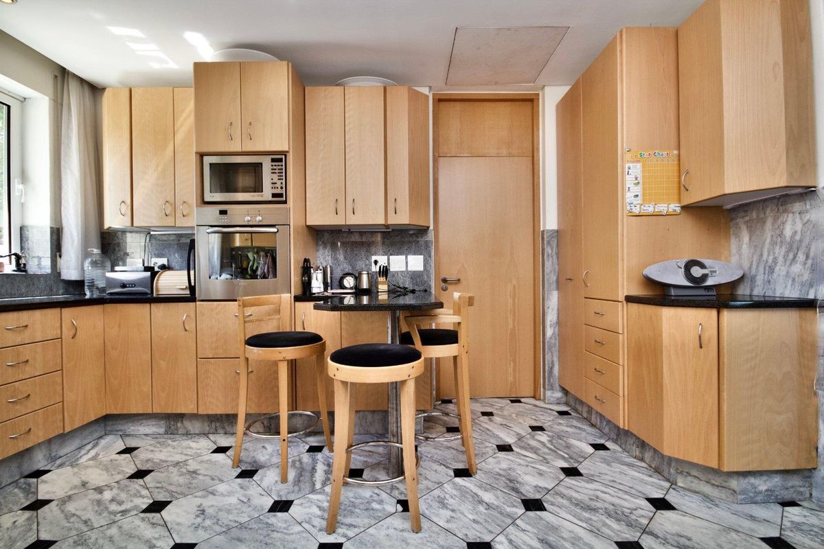 A functional kitchen featuring light wood cabinetry, granite countertops, marble flooring, and integrated appliances including an oven and microwave.