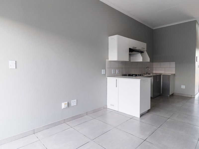 Open-plan kitchen area featuring white cabinetry, a gas hob, extractor fan, and tiled flooring, leading directly to an outdoor balcony space.