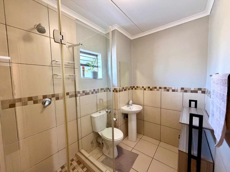 A functional bathroom featuring a glass-enclosed shower, pedestal sink, and neutral ceramic tiling throughout.