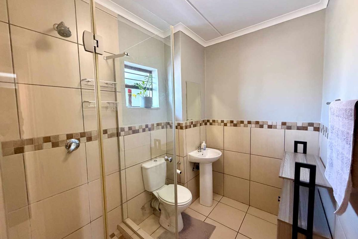 A functional bathroom featuring a glass-enclosed shower, pedestal sink, and neutral ceramic tiling throughout.