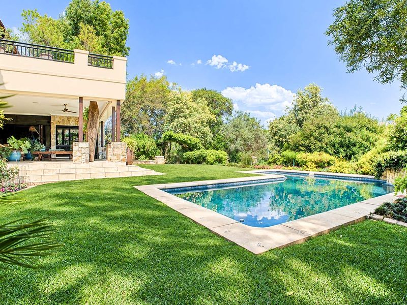 A well-maintained backyard featuring a swimming pool, stone-paved patio, covered outdoor living area, and lush landscaped garden.