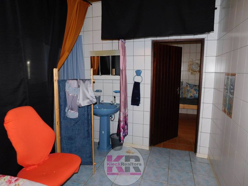 A dated bathroom featuring blue pedestal sink, tiled walls and flooring, with an adjacent room visible through the doorway.