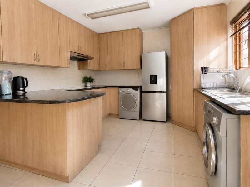 Functional kitchen featuring light wood laminate cabinetry, granite countertops, tiled flooring, and integrated space for laundry appliances.