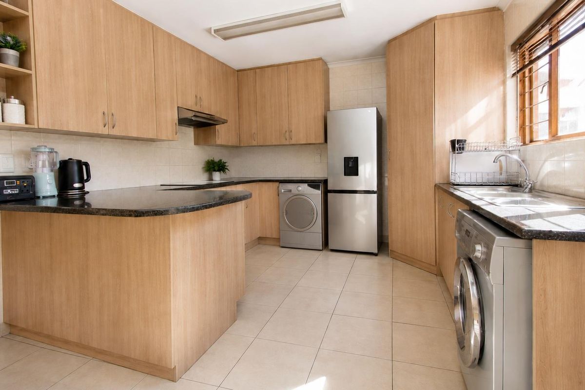 Functional kitchen featuring light wood laminate cabinetry, granite countertops, tiled flooring, and integrated space for laundry appliances.