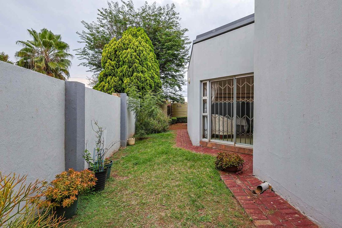 A side garden area featuring a brick pathway, boundary wall, and access to the interior via a sliding door with a security gate.