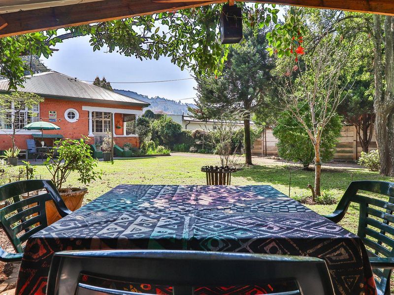 A covered patio area overlooking a spacious, well-maintained garden and the rear brick facade of the house.