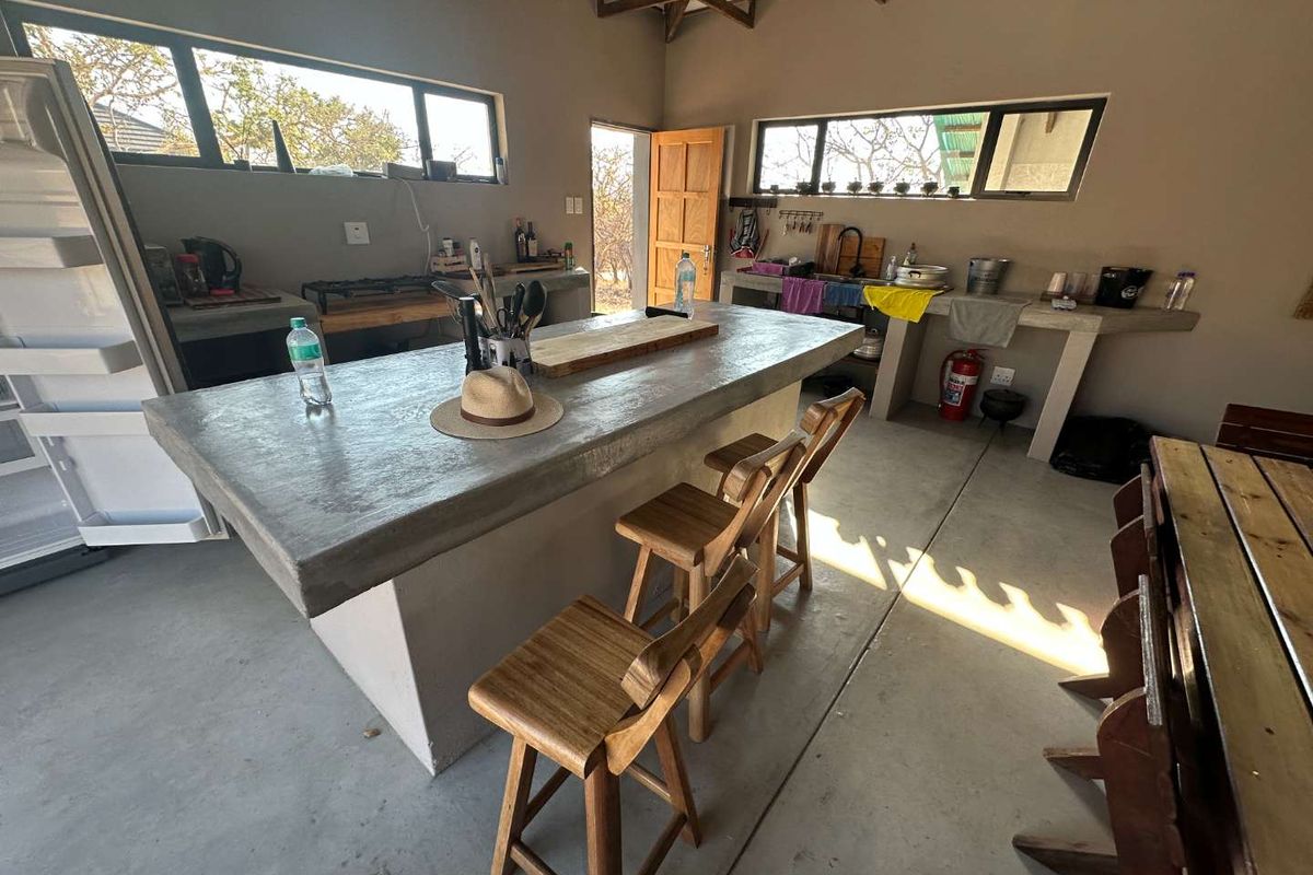 Open-plan kitchen area featuring concrete countertops, exposed timber roof trusses, and polished concrete flooring, providing a rustic and functional cooking space.