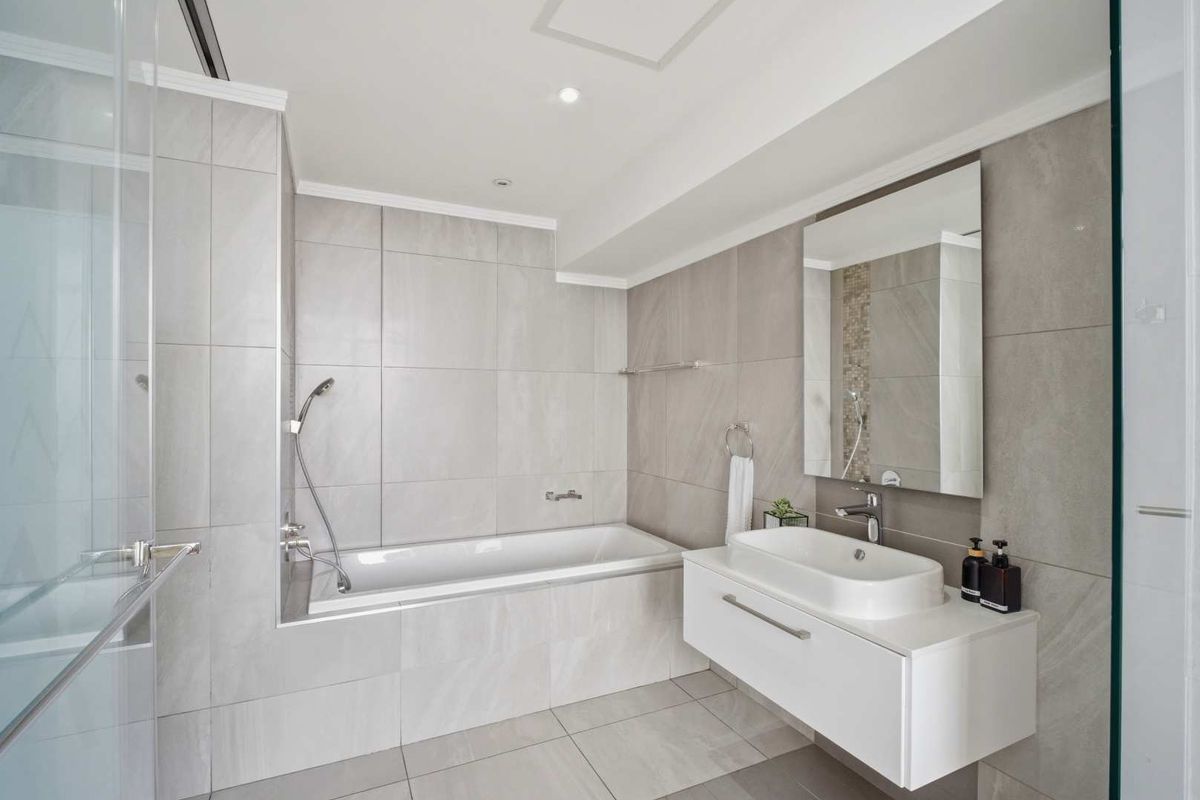 Modern bathroom featuring large format grey wall tiles, a floating vanity with a vessel sink, and a built-in bathtub with a shower mixer.