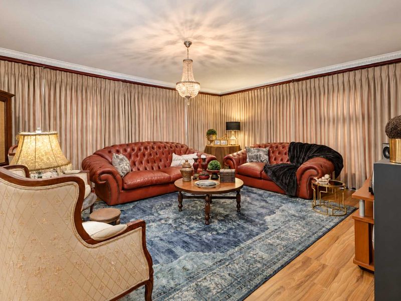 A formal living room featuring crown molding, laminate flooring, and a central crystal chandelier, creating a classic and well-maintained atmosphere.