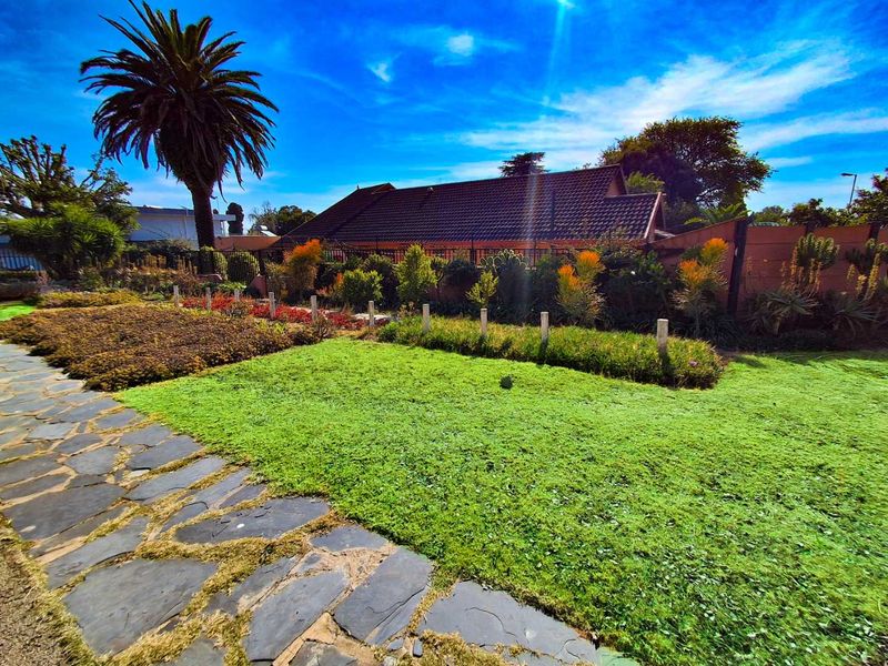 A well-maintained garden featuring a stone paved pathway, lush lawn, and established landscaping with a view of the property's rear exterior.
