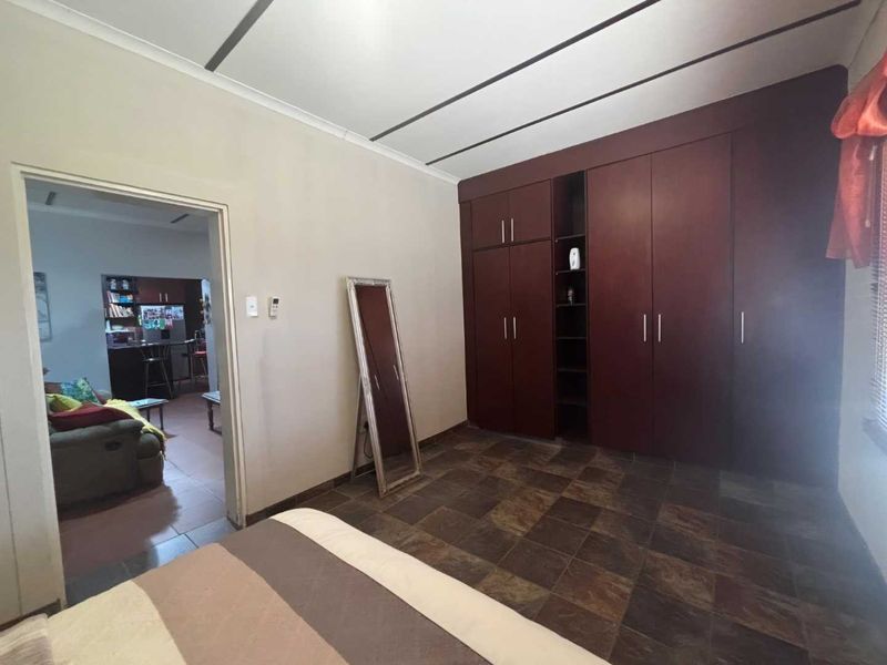 A bedroom featuring dark wood built-in cupboards and tiled flooring, with an open doorway leading to an adjacent living area.