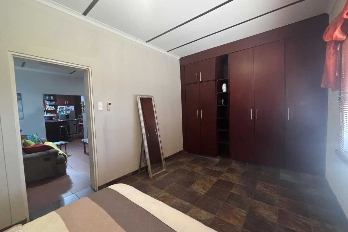 A bedroom featuring dark wood built-in cupboards and tiled flooring, with an open doorway leading to an adjacent living area.