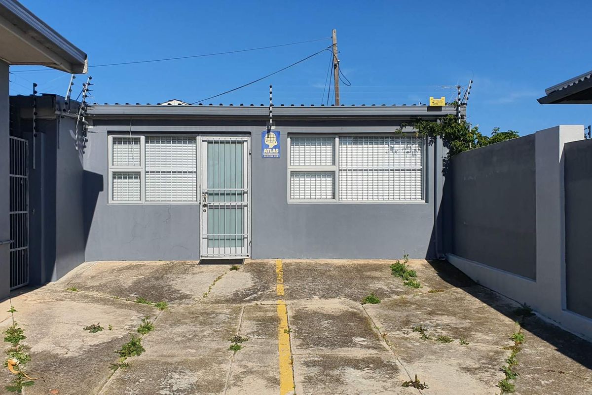 Rear exterior view of the office building featuring a paved courtyard area, security gate, and perimeter electric fencing.