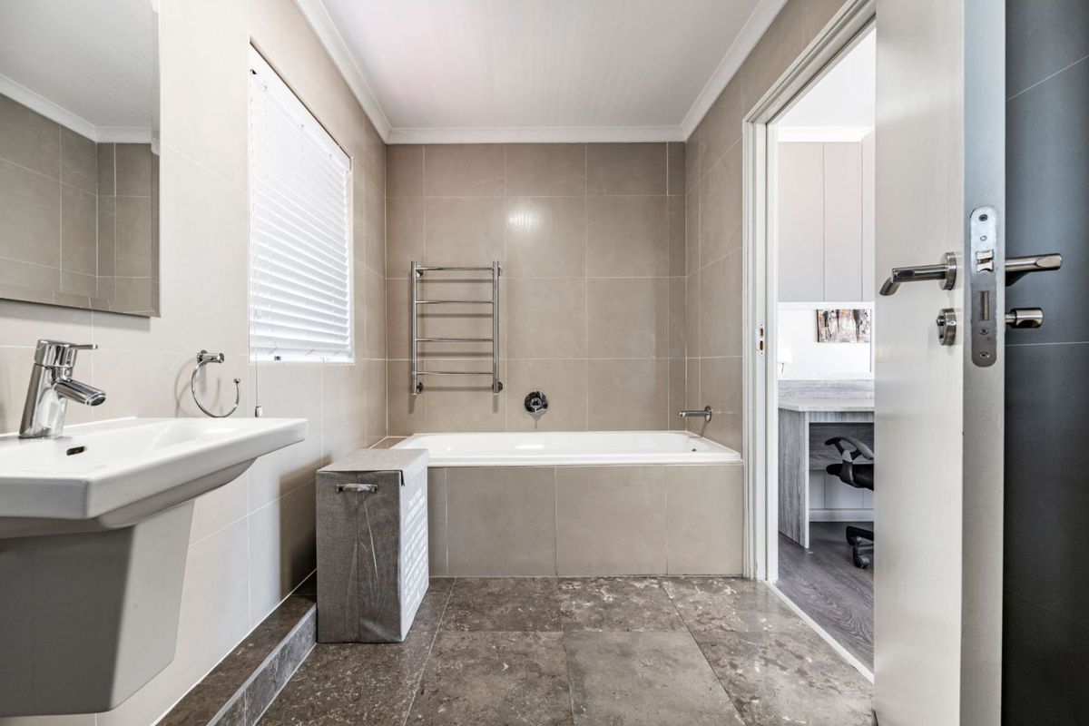 Modern bathroom featuring a built-in bathtub, pedestal basin, and heated towel rail with neutral wall and floor tiling.