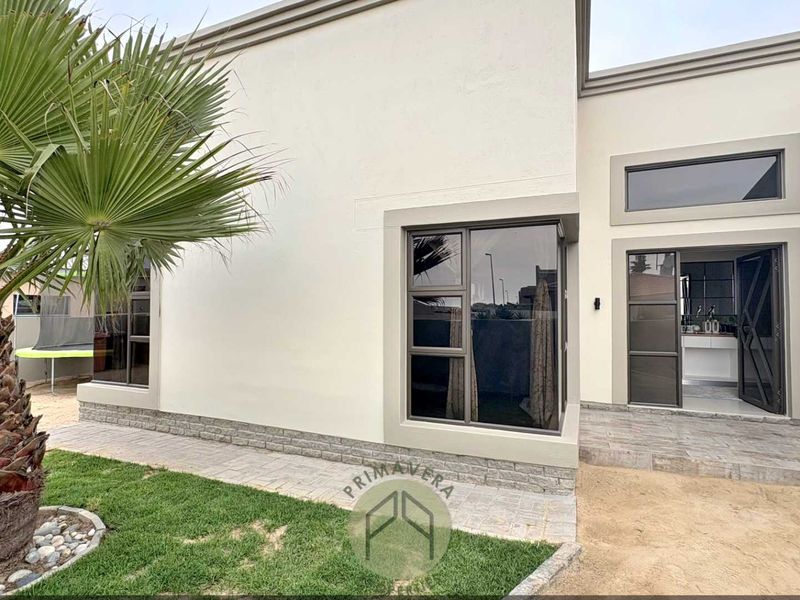 Rear exterior view of the property featuring modern stone cladding, aluminium window frames, and a paved patio area leading into the home.