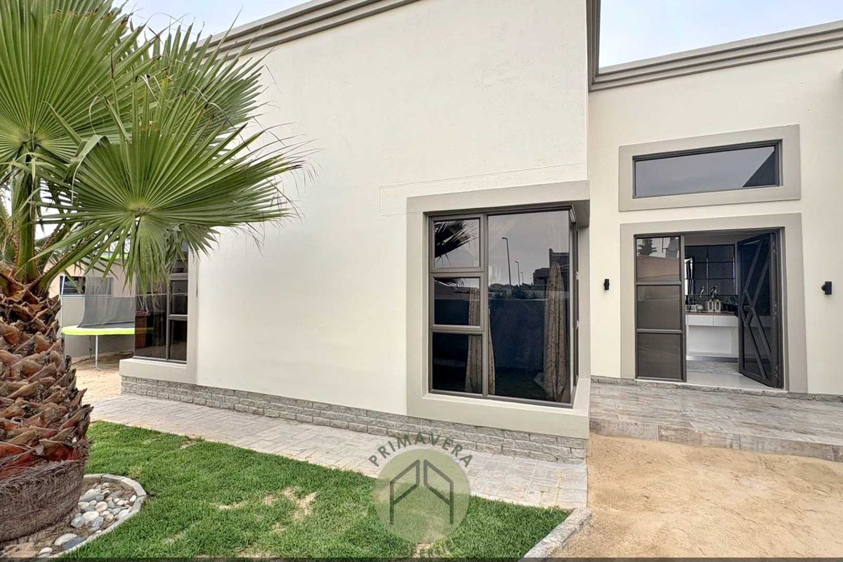 Rear exterior view of the property featuring modern stone cladding, aluminium window frames, and a paved patio area leading into the home.