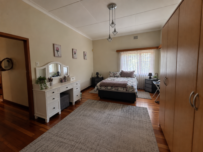 A spacious bedroom featuring polished hardwood flooring, a large built-in wardrobe, and a central pendant light fixture.