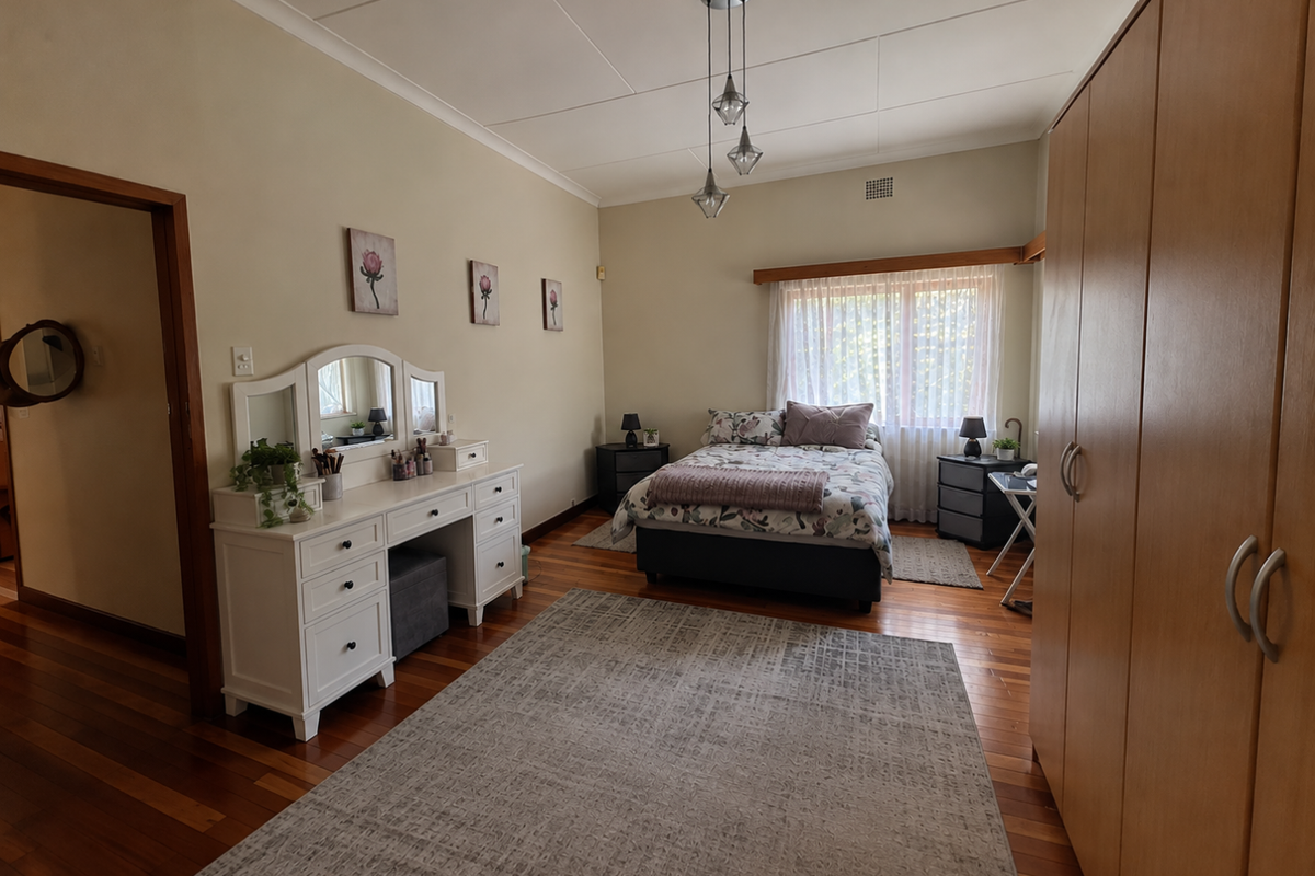 A spacious bedroom featuring polished hardwood flooring, a large built-in wardrobe, and a central pendant light fixture.