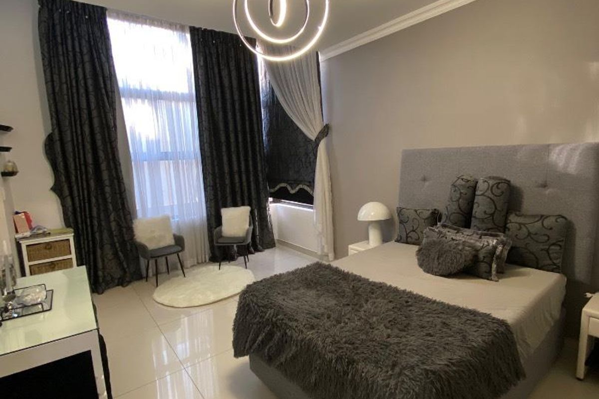 A spacious bedroom featuring large windows with floor-to-ceiling curtains, modern tiled flooring, and a contemporary circular pendant light fixture.