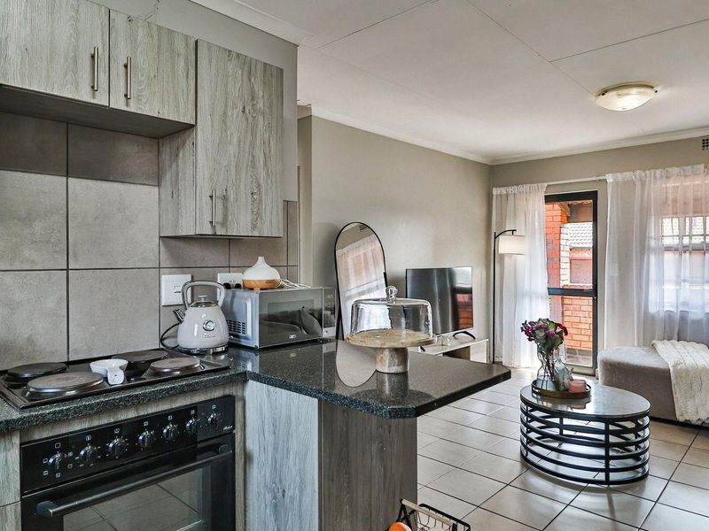 Open-plan living area featuring a modern kitchen with granite countertops, built-in cabinetry, and an electric stove, flowing into a bright, tiled lounge space.