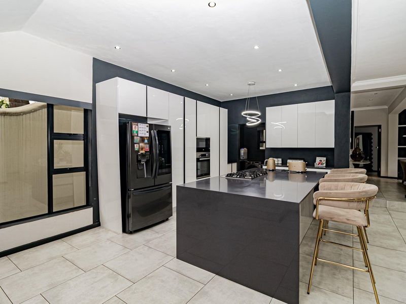 Modern kitchen featuring high-gloss cabinetry, a large central island with a gas hob, stone countertops, and sleek recessed lighting.