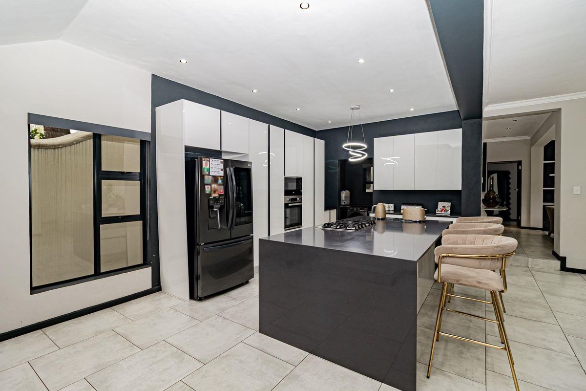 Modern kitchen featuring high-gloss cabinetry, a large central island with a gas hob, stone countertops, and sleek recessed lighting.